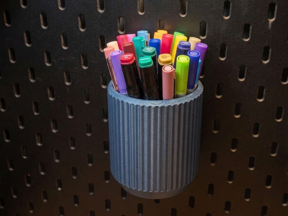 Blue fluted holder filled with colourful markers on an IKEA SKÅDIS pegboard